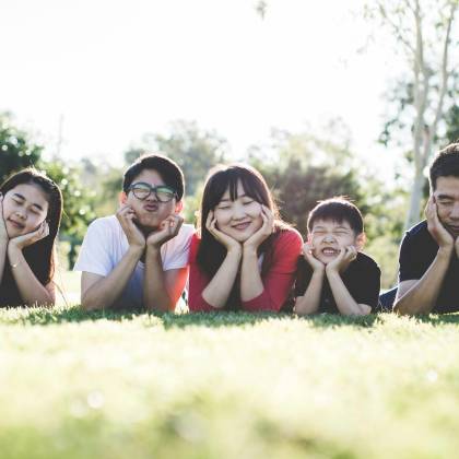 Asian Family Posing Happily On The Grass In A Sunny Park, Showcasing Love And Togetherness.