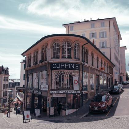 Explore A Bustling Street Corner In Lausanne Featuring Classic European Architecture And Urban Life.