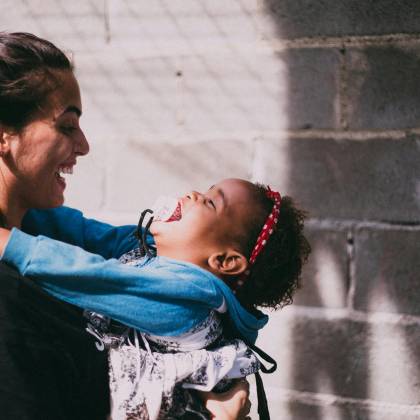 A Mother And Her Child Joyfully Embrace, Sharing A Moment Of Happiness Outdoors.