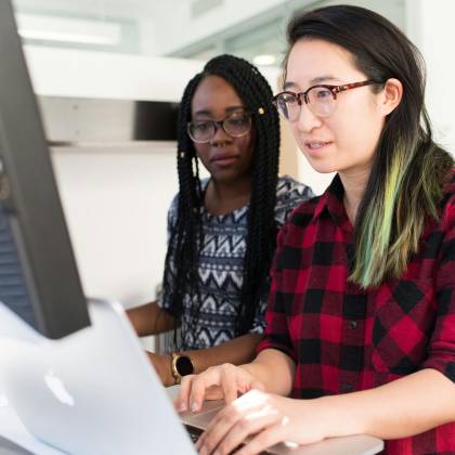 Two Women Working On A Computer Project Together In An Office Setting.