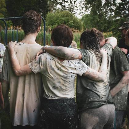 Group Of Teenagers Bonding In A Muddy Team Building Exercise Outdoors.