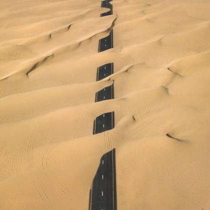Stunning Aerial Shot Of A Road Cutting Through The Sand Dunes In Dubai's Desert.