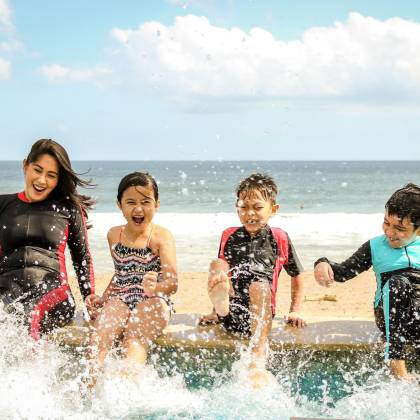 A Family Having Fun Splashing Water Near The Seashore On A Sunny Day In Bali, Indonesia.