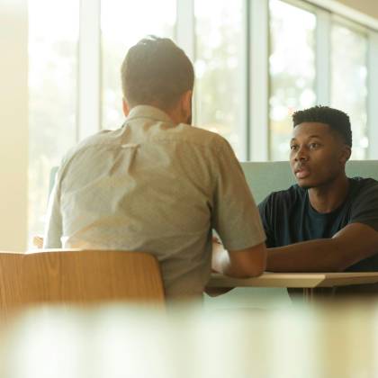 Two Men Sitting At A Table In A Modern Office Space During The Day.