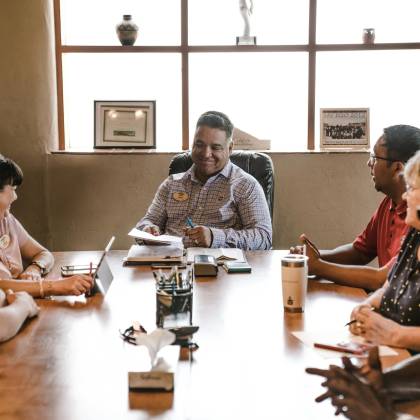 A Diverse Group Of Adults In A Collaborative Team Meeting Inside A Well Lit Office Room.