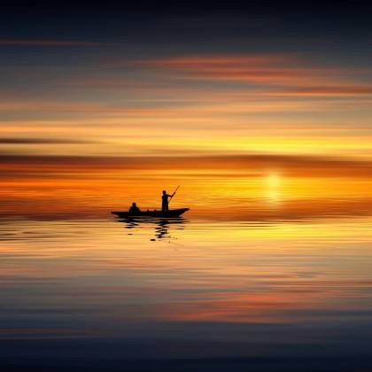 Silhouette Of Two People In A Boat Against A Vibrant Sunset Over Calm Waters. Tranquil Scene.