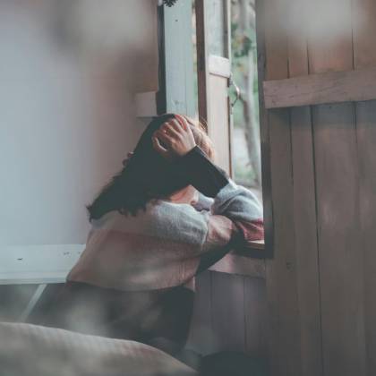A Woman Sits Indoors Gazing Thoughtfully Out Of A Window, Evoking Emotions Of Loneliness And Reflection.