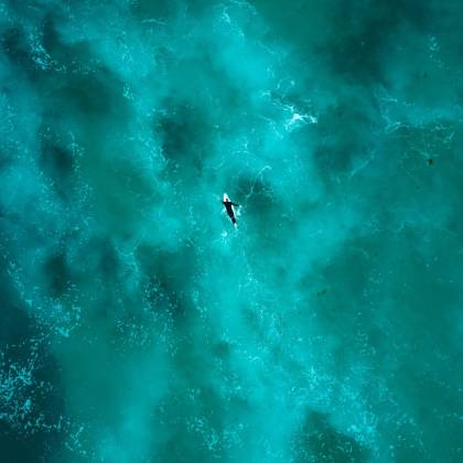 Breathtaking Aerial Shot Of A Lone Surfer Navigating The Vibrant Turquoise Waters Near Sydney.