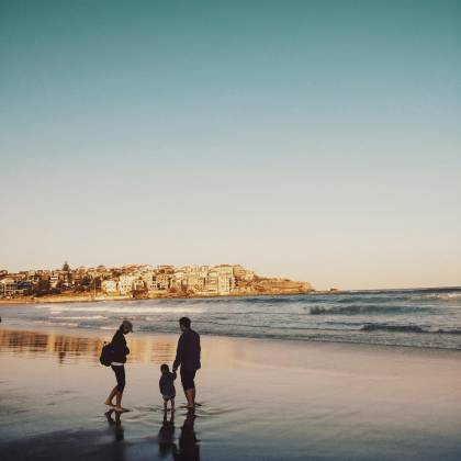 A Family Enjoying A Peaceful Walk Along Bondi Beach During Sunset, With City Views In The Background.
