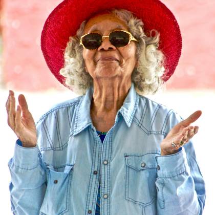 Joyful Senior Woman Wearing A Vibrant Red Hat And Sunglasses, Expressing Happiness Outdoors.