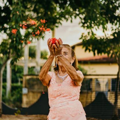 Elderly Woman In Elegant Dress Tossing Flowers, Enjoying Outdoor Leisure.