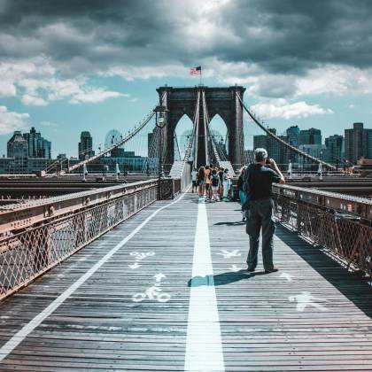 Iconic View Of Brooklyn Bridge Filled With Pedestrians Under Dramatic Skies.