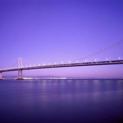 Beautiful View Of The Bay Bridge Lit Up At Twilight Against A Vibrant Purple Sky.