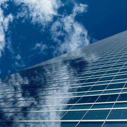 Low Angle View Of A Modern Skyscraper With Reflective Glass Windows Against A Blue Sky.