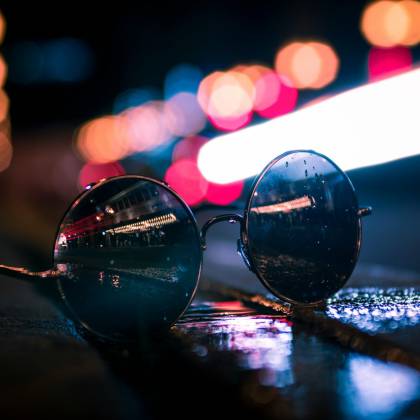Round Sunglasses Reflecting Vibrant City Lights On A Wet Street At Night.