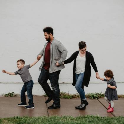 A Joyful Family Walking Together Outdoors, Holding Hands In A Playful And Happy Moment.
