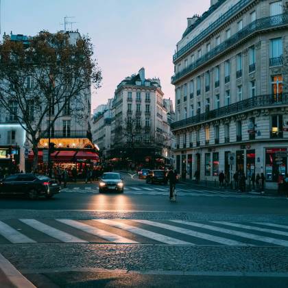 Urban Street Scene At Dusk With Cars And Pedestrians In A Bustling City Intersection.
