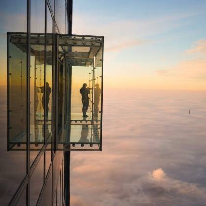 Silhouette Of A Person On Chicago Skydeck Overlooking A Foggy Skyline At Sunset.