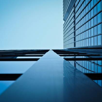 Low Angle View Of A Modern Skyscraper With Reflective Glass Facade And Blue Sky.