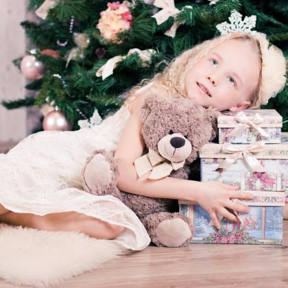A Joyful Child Hugging A Teddy Bear Near A Holiday Tree With Gifts.