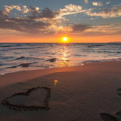 Beautiful Sunset Over Ocean With A Heart Shape In The Sand, Perfect For Romantic Themes.