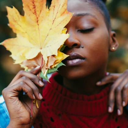 Close Up Portrait Of A Woman Holding A Large Autumn Leaf Outdoors.