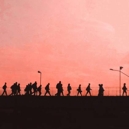 Dramatic Silhouettes Of People Walking Across A Bridge Against A Warm Sunset Sky.