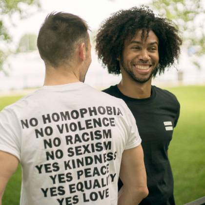Two Men Smiling In A Park, Wearing T Shirts Promoting Equality And Kindness.