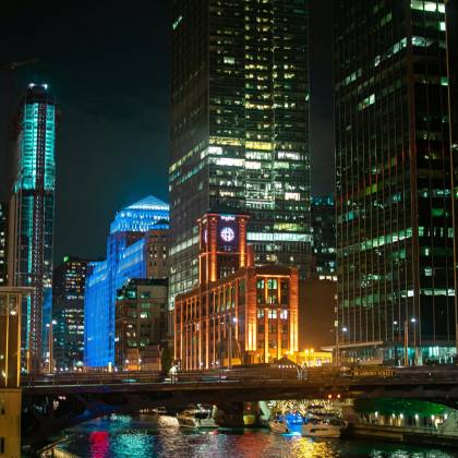 Mesmerizing Night View Of Chicago's Illuminated Skyline With Boats On The River, Capturing Urban Vibrancy.