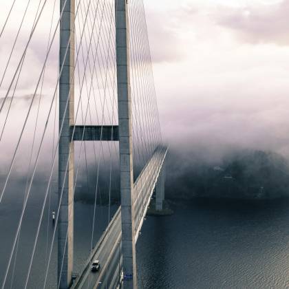 A Dramatic View Of A Fog Covered Suspension Bridge With Cables And The Ocean Below.
