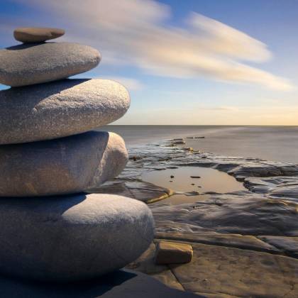A Serene Stack Of Stones On The Rocky Seashore During A Peaceful Sunrise, Embodying Balance And Zen.