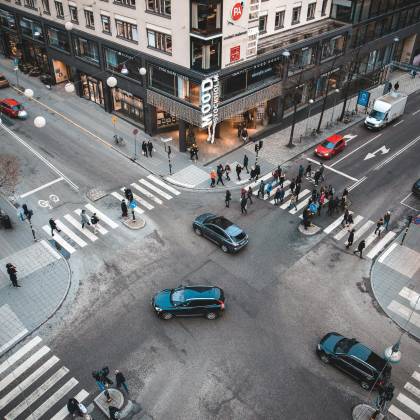 A Bustling Stockholm Street Intersection With Pedestrians And Vehicles On A Sunny Day.