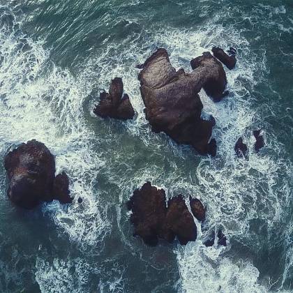 Dynamic Aerial View Of Ocean Waves Crashing Against Rocky Structures, Captured From Above.