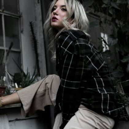 Stylish Woman In Plaid Shirt Poses In Urban Setting, Showcasing Modern Fashion And Style.