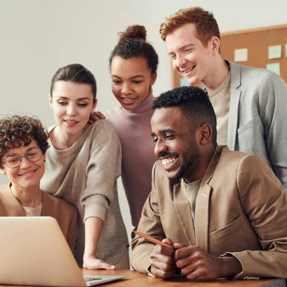 A Group Of Diverse Young Professionals Happily Collaborating Around A Laptop Indoors.