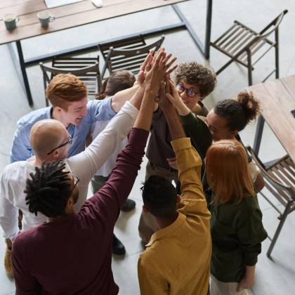 A Diverse Group Of Professionals High Fiving In A Modern Office, Showcasing Teamwork And Collaboration.