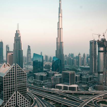 Aerial View Of Dubai's Skyline With Burj Khalifa And Intricate Highway System At Sunset.