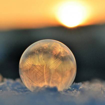 A Frozen Soap Bubble On Snow Captures Crystalline Patterns Against A Sunrise Backdrop.