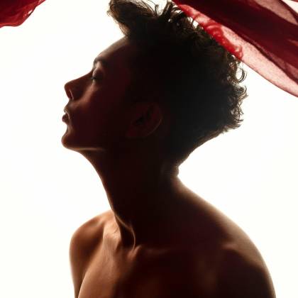 Silhouette Of A Topless Man With Flowing Red Fabric. Dramatic Lighting Creates An Artistic Mood.