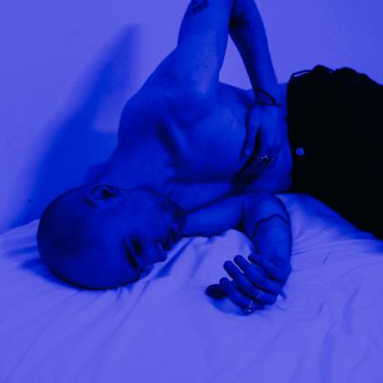 A Shirtless Man Lies On A Bed In Blue Light, Expressing Deep Emotion And Contemplation.