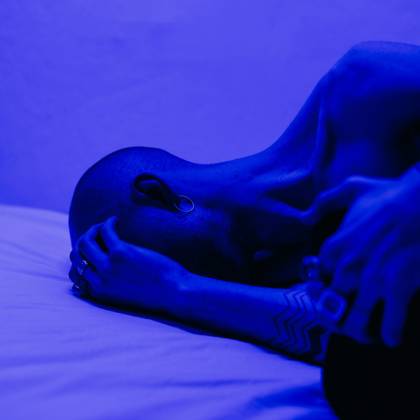 A Tattooed Man Lying In Blue Light, Symbolizing Isolation And Stress.