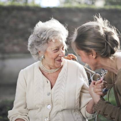 Joyful Interaction Between An Elderly Woman And Her Granddaughter In A Sunny Outdoor Setting.