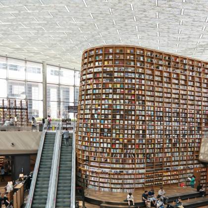 Interior View Of A Modern Library In Seoul With A Vast Bookshelf And Escalators Under A Glass Ceiling.