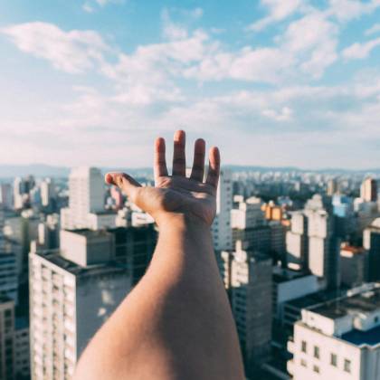 An Outstretched Hand Reaching Towards A Sunny Cityscape, Capturing The Vibrant Skyline And Skyscrapers.