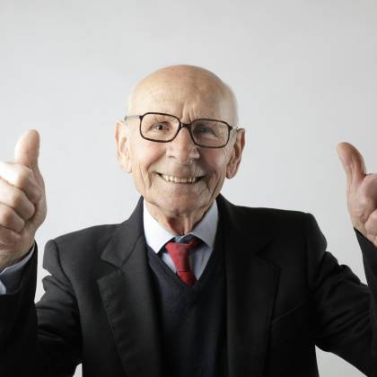 Cheerful Elderly Man In Suit Giving Thumbs Up, Symbolizing Success And Approval.
