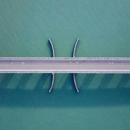 Aerial Shot Of A Bridge Over Clear Blue Water, Showcasing Modern Architecture And Symmetry.