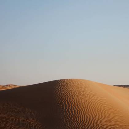 Captivating View Of A Sunlit Sand Dune With Clear Blue Sky Background, Showcasing Natural Desert Beauty.