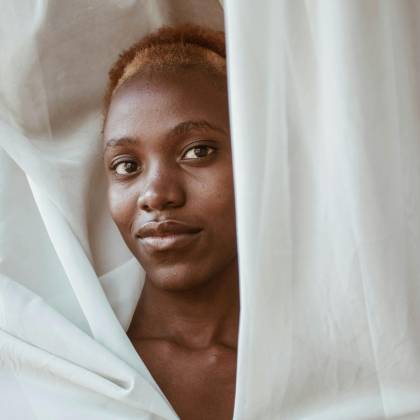 Captivating Natural Portrait Of An African Woman Peeking Through Draped Fabric With Serene Expression.
