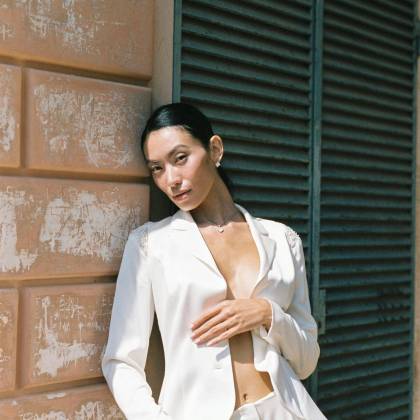 Elegant Portrait Of An Asian Woman In A Stylish White Suit Against A Textured Wall.