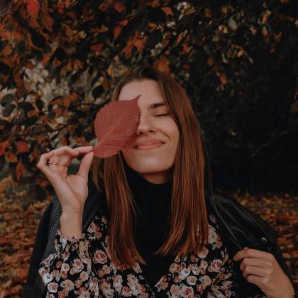 Woman In Floral Dress Smiling With Leaf Over Eye In Autumn Setting.